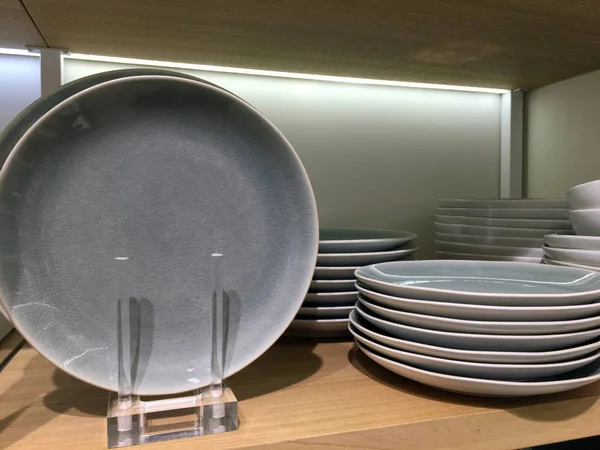 Gray ceramic plates on a shelf in a store. Designer ceramic plates with a pattern. Table setting, tableware and eating concept. Various Types Of fashionable set of dishes on supermarket shelves