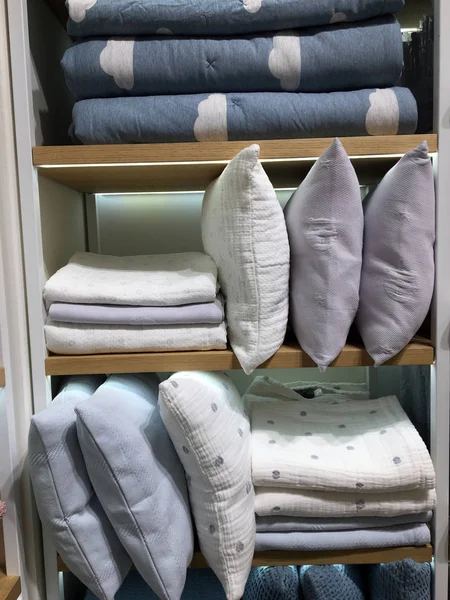 Stack of blankets and pillows are on the shelf. Folded winter clothes on shelves in wardrobe. Towels for sale in store that sells bed, table and bath articles. Merchandise arranged in shop interior