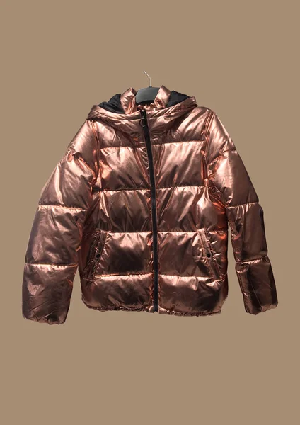 Shiny gold puffer jacket isolated on brown background. Fashionable winter jacket. Banner concept. Copy space