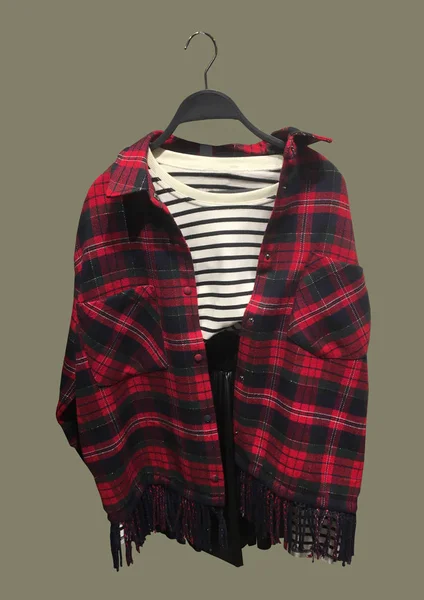 Clothes on a hanger isolated on brown background. Striped sweater and red plaid shirt. Women's look. Composition of clothes. Flat lay, top view, copy space. Winter clothes pattern