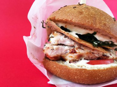 Kırmızı arka planda kızarmış tavuk burgeri. Hamburgerin beyaz kağıdıyla yakın plan görüntüsü. Geleneksel fast food. Tasarım için alanı kopyala. Sağlıksız yiyecekler. Lezzetli ızgara ve tavuk burger.