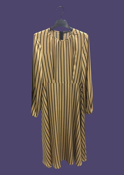 Beautiful elegant beige striped dress on a hanger isolated on purple background. Long silk dress with long sleeves. Composition of clothes. Flat lay, top view, copy space. Clothes pattern