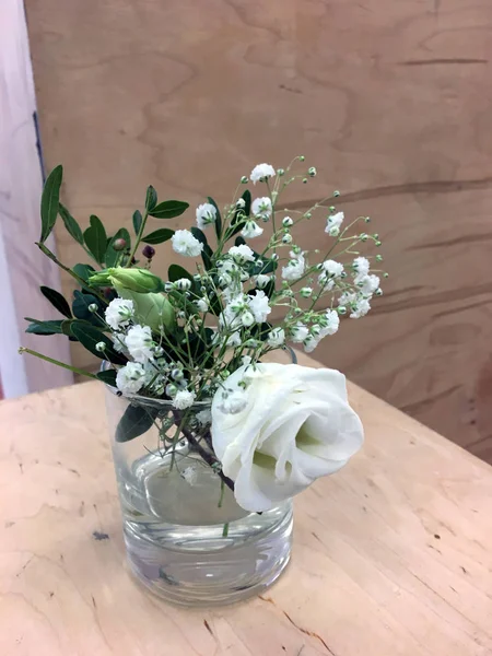 Small glass vase with a bouquet of roses and dried flowers on wooden box. Wedding decor. Small glass vase with a rose and green branches. Interior with flowers