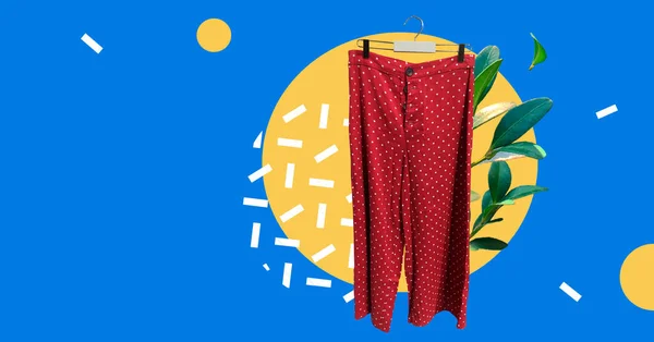 Red women's cropped button-up polka dot trousers on hanger with fresh plants isolated on abstract colorful background. Composition of clothes. Collage sale clothes banner. Fashion concept
