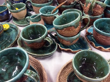 Beyaz kumaşta yeşil kil sürahiler. Terracotta seramik tabaklar. Mutfak için bulaşık koleksiyonu mağazada satılıyor. Ulusal çömlek. Çevre dostu seramik kaplar