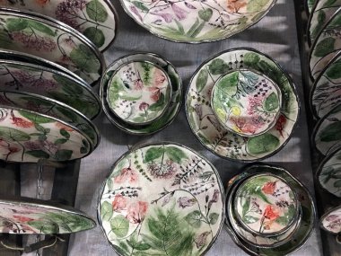 Elle boyanmış porselen tabaklar. Oval şekilli Derin Seramik Tasarımcı Tabakları. Mağazada çiçekli modern seramik oval plakalar çiziliyor. Dışarıda gümüş boyalı bir kase var. Modern el yapımı seramik sofra takımı