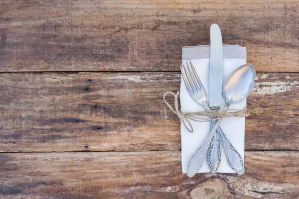 Table setting with silver cutlery and napkin on wood background, top view