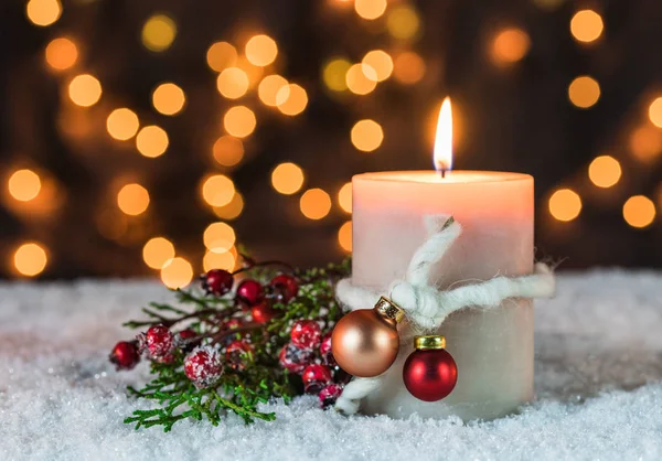 Traditional Christmas time holiday season candle with decoration and ornament over snow with blurred light background