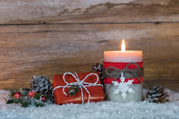 Christmas decoration with candle and gift box on snow with wood background