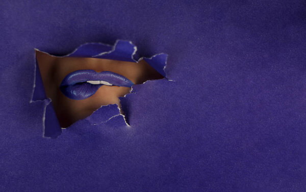 Beautiful plump, bright purple lips fall into the slit of colored paper. Cosmetics, cosmetics, beauty salon, makeup artist, lip gloss, beautiful teeth, sales.