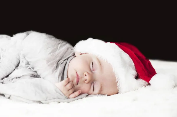 白い格子縞の灰色の布に包まれた白い毛布で寝ているサンタ帽子で非常に美しい 明るい 幸せな赤ちゃん — ストック写真
