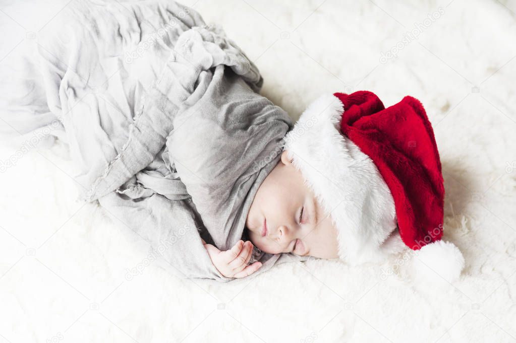 very beautiful bright happy little baby in Santa hat sleeping on white plaid wrapped in gray fabric