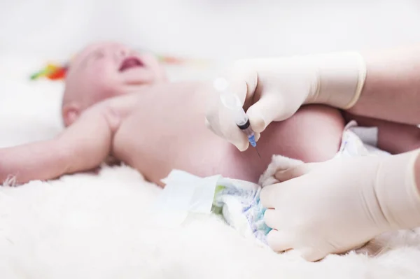 A very small child, a baby, is lying in the doctors office and the doctor makes an injection. — Stock Photo, Image