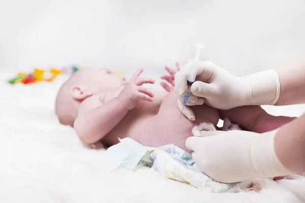 A very small child, a baby, is lying in the doctors office and the doctor makes an injection. Stock Image