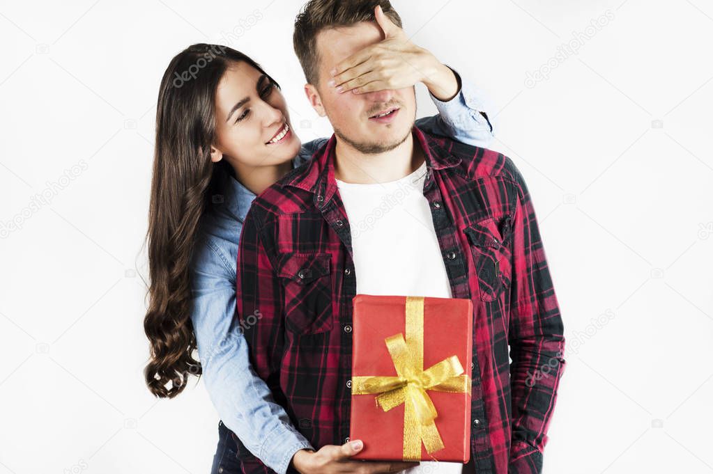 A young beautiful girl makes a surprise to her boyfriend and gives him a gift by covering his eyes with a hand. They laugh emotionally.