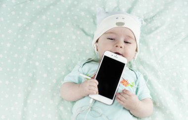 Parlak küçük güzel yeni doğan bebek bir telefon el ve kulaklık ile müzik dinliyor ve telefon nibbles