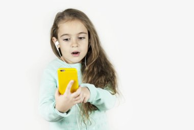 Parlak güzel küçük kız kulaklık telefon ile izole bir arka plan üzerinde duygusal şaşırır.