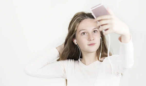 Ellerini bir telefon ile kulaklık parlak güzel kız müzik dinliyor ve fotoğraf izole bir arka plan üzerinde yapar.