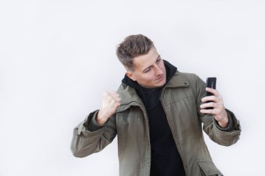 Genç adam gri arka plan üzerinde izole portresi, sergilenen bu onun akıllı telefon, medya içeriği Web'den tarafından etkilendim heyecanlı arıyorum