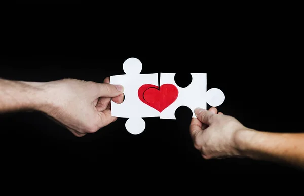 Puzzle with a red heart in the hands of a loving couple. Valentine\'s day concept.On a black isolated background