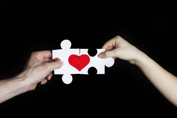 Rompecabezas con un corazón rojo en las manos de una pareja amorosa. Concepto del día de San Valentín. Sobre un fondo negro — Foto de Stock