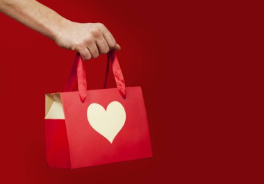 A girl holds a gift with a heart closeup on an isolated red background. Valentine day concept. Lovers day. clipart