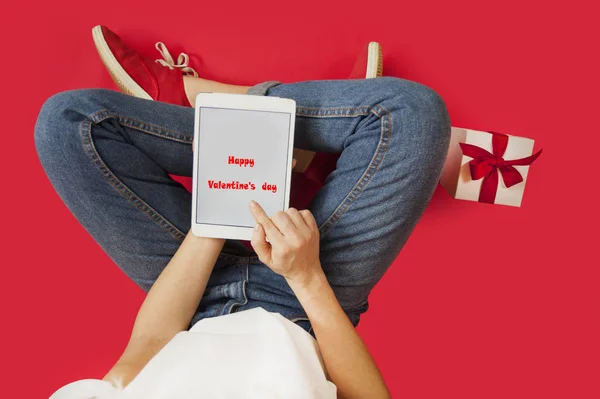 Ragazza con ipad in mano, regali, sconti, seduta su uno sfondo rosso isolato, San Valentino . — Foto Stock