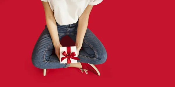 Κορίτσι με λευκό δώρο με κόκκινο φιόγκο κάθεται σε ένα απομονωμένο κόκκινο backgroundvalentines μέρα. — Φωτογραφία Αρχείου