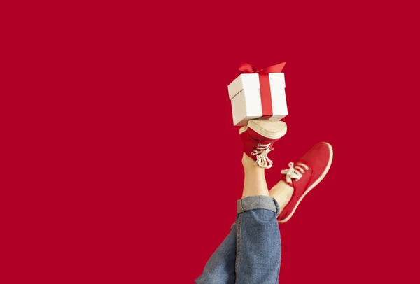 Feet with a gift for the holidays on an isolated red background, a girl with a gift, giving gifts, discounts. Valentines Day. — Stock Photo, Image