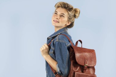 Bir kot ceket mavi bir arka plan üzerinde stüdyoda onun omuzlarında bir sırt çantası ile mutlu güzel öğrenci kız. Eğitim ve öğrenme kavramı.