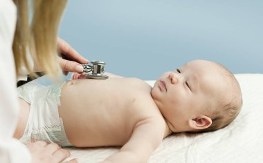 Çok küçük bir çocuk, çocuk, doktor ofisinde yatıyor ve Doktor akciğerler, kalp dinler. Çocuk Sağlığı kavramı