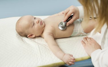 Çok küçük bir çocuk, çocuk, doktor ofisinde yatıyor ve Doktor akciğerler, kalp dinler. Çocuk Sağlığı kavramı