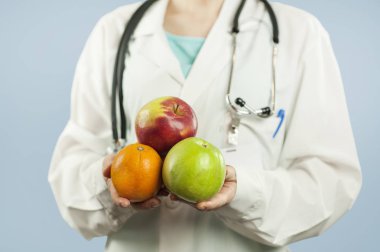 güzel kız doktor beslenme uzmanı izole mavi zemin üzerine elinde meyve ile. Sağlıklı beslenme kavramı