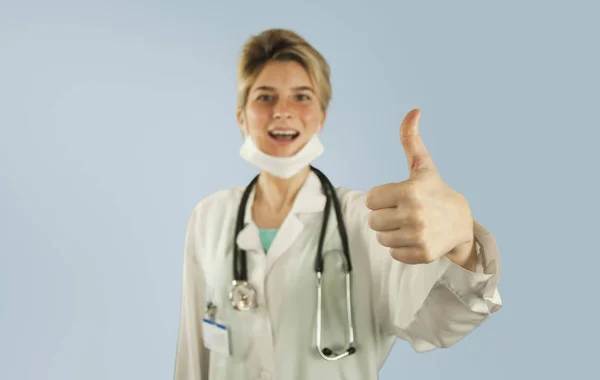 年轻的医生女孩在蓝色被隔绝的背景显示拇指 概念医学与健康 — 图库照片