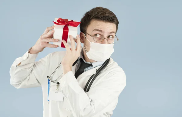 年轻的医生学生与礼物在他的手在一个孤立的蓝色背景 概念医学和健康 假期和礼物 — 图库照片