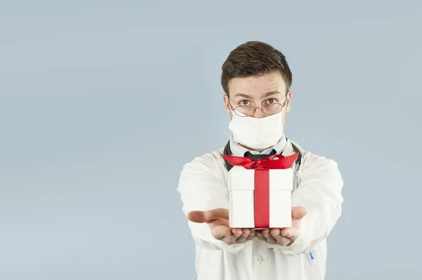 young doctor student with a gift in his hands on an isolated blue background.concept medicine and health, holidays and gifts