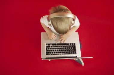 güzel bebek çocuk elinde bir dizüstü bilgisayar ile oturma ve Internet üzerinde kırmızı bir arka plan hakkında bilgi arıyorum. Modern çocuk kavramı