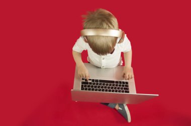 güzel bebek çocuk elinde bir dizüstü bilgisayar ile oturma ve Internet üzerinde kırmızı bir arka plan hakkında bilgi arıyorum. Modern çocuk kavramı