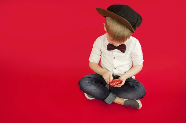 for holidays, lovers day and mothers day, baby boy sits on a red background with a red heart in his hands. The concept is to give gifts and love