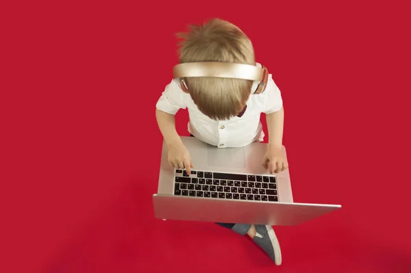 güzel bebek çocuk elinde bir dizüstü bilgisayar ile oturma ve Internet üzerinde kırmızı bir arka plan hakkında bilgi arıyorum. Modern çocuk kavramı
