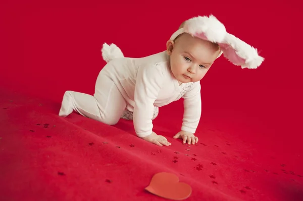 Pequeno bebê recém-nascido bonito rasteja em um fundo vermelho isolado com um presente em kayts komelyum. Conceito feriados e trajes — Fotografia de Stock