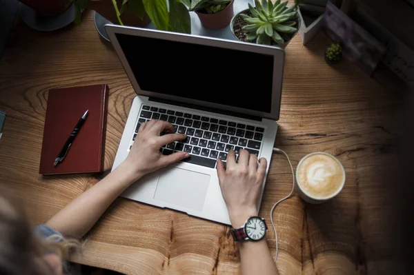 Uma garota em um café com um laptop funciona em um lugar acolhedor com uma xícara de café, tem prazer. O conceito de freelancer — Fotografia de Stock
