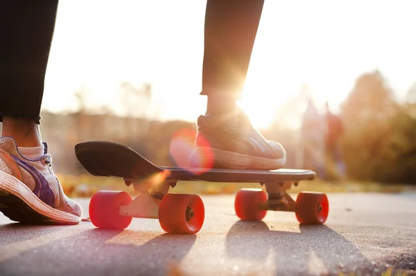 若い女の子の足のスケート ボード上の道の夕日に動き。スポーツの概念 — ストック写真