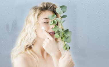 Duş aldıktan sonra bir genç kız bir nemlendirici vücut ve yüz kremi bir mavi izole arka plan üzerinde kullanır. Cilt Bakımı ve kozmetik kavramı