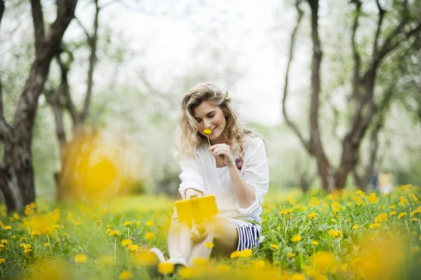Güzel saçlı güzel sarışın kız karahindiba tarlasında oturur ve selfie çeker. — Stok fotoğraf