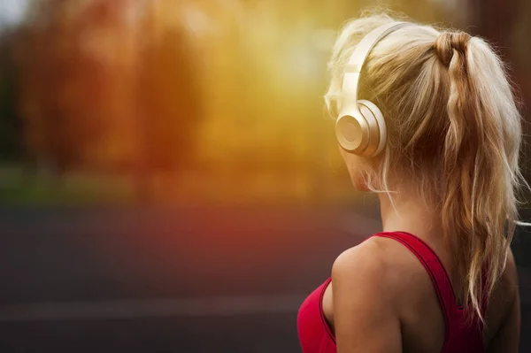 Glückliche, athletische junge Frau, in Sportbekleidung, im Freien stehend und mit Kopfhörern Musik hörend, vor dem Training — Stockfoto