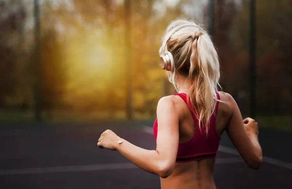 Mujer joven atlética feliz, en ropa deportiva, de pie al aire libre y escuchando música con auriculares, antes de entrenar —  Fotos de Stock