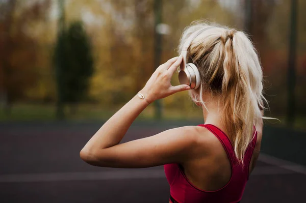 Gelukkige atletische jonge vrouw, in sportkleding, buiten staan en luisteren naar muziek met een koptelefoon, voor de training — Stockfoto