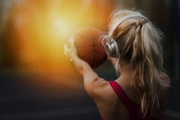 Портрет великолепной концентрированной красивой сильной спортивной женщины на открытом воздухе, позирующей, слушая музыку с наушниками, держащими баскетбол. — стоковое фото