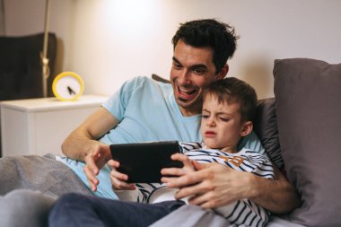baba ve oğlu evde tablet üzerinde oyun oynuyor